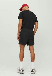 Schwarzes T-Shirt und passende Shorts aus Baumwollmischung, mit einem elastischen Bund. Eine rote Mütze rundet das lässige Outfit ab.