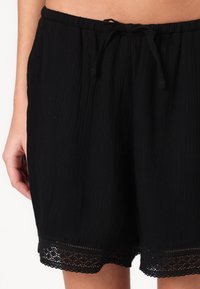 Pantaloni corti neri in tessuto testurizzato, con un elastico in vita e un cordoncino, e una rifinitura in pizzo all'orlo. Vestibilità casual.