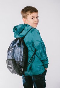 Der drawstring Rucksack im Batman-Design hat schwarz-blaue Grafiken, eine glänzende Textur und eine vordere Reißverschlusstasche.