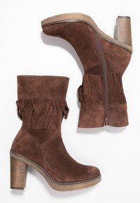 Stivaletti alla caviglia in suede marrone con dettaglio a frange, punta arrotondata e tacco impilato strutturato. Dotati di cerniera laterale per una facile calzata.