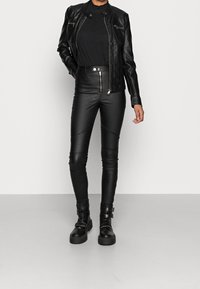 Schwarze Lederjacke mit Reißverschlusstaschen, strukturiertes schwarzes Oberteil, elegante schwarze Lederhose mit Nähten und klobige schwarze Stiefel mit Hardware-Details.