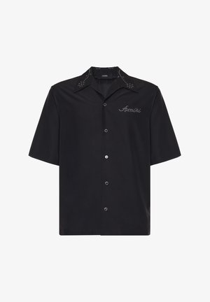 Camisa negra de manga corta con botones, cuello puntiagudo, tachuelas plateadas en el cuello y logotipo "Amiri" en tachuelas plateadas en el pecho.