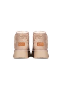 Botas de tobillo de ante beige con un talón reforzado, forro suave y suela de goma, con una etiqueta de logo marrón en la parte posterior.