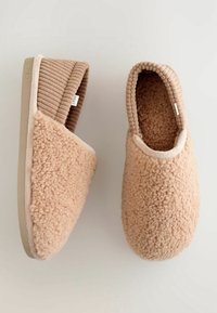 Chaussons marron clair et duveteux avec une surface extérieure douce et texturée, et un col côtelé de type chaussette beige. Semelle plate pour un port facile à l'intérieur.