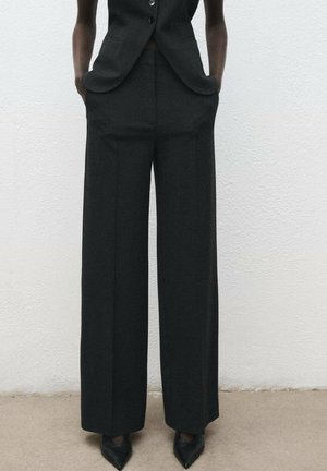 Black wide-leg trousers in a textured fabric, featuring side pockets and a tailored fit, paired with pointed black shoes.