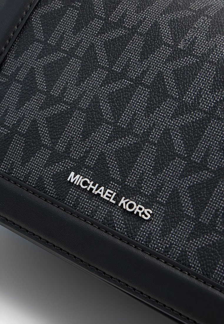 Portefeuille en cuir noir avec texture en toile, présentant un motif décoratif et un logo métallique "MICHAEL KORS" dans le coin inférieur droit.