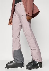 Világos rózsaszín sínadrág szürke szegéllyel a szárvégnél, karcsúsított fazonban, cipzáras zsebbel és vízálló anyagból.