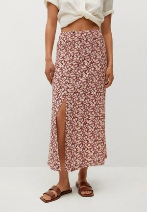 Kvinde iført et blomsterprintede midi-nederdel med højtaljet, knapper foran og en frontslids, hvid cropped skjorte med bindebånd og brune flade sandaler.