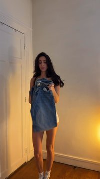 Jeansjacka med ljus tvätt, med knäppning fram och två bröstfickor, hålls av en person i en vit topp och mönstrade strumpor.