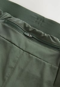 Mørkegrønne træningsshorts har et glat stof, elastisk talje og en lynlåslomme på ryggen med en skjult lynlås.