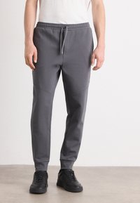 Pantaloni sportivi gri cu talie elastică, detalii subtile de cusătură și glezne strânse, asortați cu adidași negri.