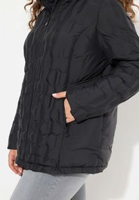 Svart puffjacka med kviltat mönster, dragkedja fram och sidofickor. Tyget verkar slätt och något glänsande.