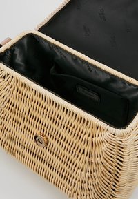 Tkana torebka ze słomy o prostokątnym kształcie, wyposażona w zapięcie na guzik w kolorze złotym oraz czarną podszewkę z materiału z wewnętrznymi przegródkami.