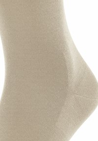 Calzino beige con una texture liscia, design a coste e tallone rinforzato. Il tessuto sembra leggero con cuciture minime.