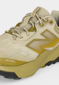 Chaussure de sport beige et jaune avec tige en mesh, fermeture à lacets, languette matelassée et étiquette « Toe Protect » à l'avant de la semelle.