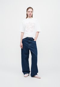 Camiseta blanca de manga corta con un diseño gráfico en rosa, combinada con unos vaqueros denim sueltos de color azul y zapatillas ligeras rosas de tipo slip-on.