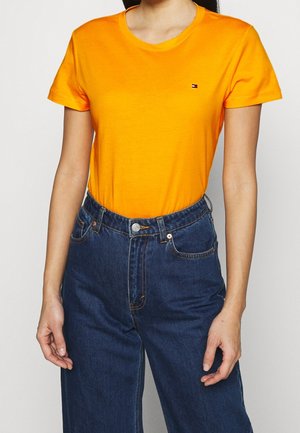 Orange bomuld t-shirt med rund hals og korte ærmer. Har en lille logo på brystet. Kombineret med højtaljede blå denimjeans.