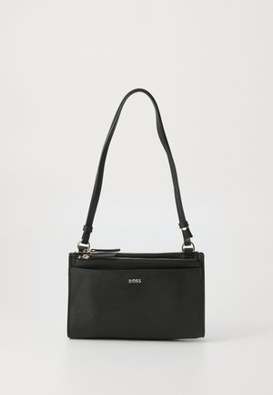 Schwarze Leder-Crossbody-Tasche mit verstellbarem Tragegurt, ausgestattet mit einem Reißverschlussfach und einem goldenen Logo auf der Vorderseite. Glatte Textur.