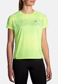 T-shirt d'athlétisme à manches courtes, de couleur jaune fluo brillante, avec un motif graphique texturé sur la poitrine, comportant des fentes sur les côtés pour un meilleur mouvement.