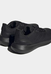 Czarne buty sportowe z teksturowaną siateczką u góry, zaokrąglonym obcasem i gumową podeszwą. Trzy równoległe paski z boku podkreślają design.