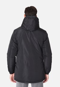 Giubbotto isolato nero con cappuccio, dotato di polsini elasticizzati e un esterno liscio. Design semplice e funzionale con una lunghezza posteriore più lunga.