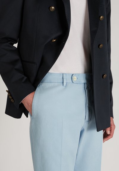 Granatowa marynarka dwurzędowa z złotymi guzikami, w komplecie z jasnoniebieskimi spodniami z zapięciem na guzik i bocznymi kieszeniami. Gładka tekstura.