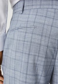 Pantaloni în carouri albastre cu un model texturat, având un buzunar la spate și o țesătură netedă. Designul include nuanțe variate de albastru deschis.