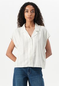 White short-sleeve shirt with vertical stripes, button front, and a soft texture. Worn with blue denim jeans.