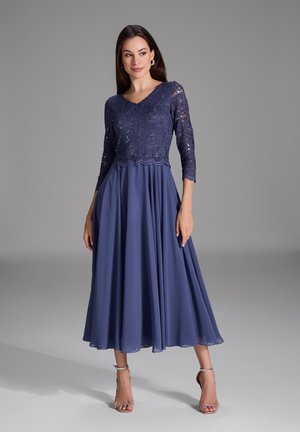 Abito blu navy con maniche in pizzo a tre quarti e una gonna fluida. Il corpino presenta una sovrapposizione in pizzo floreale e orlo a scallop.