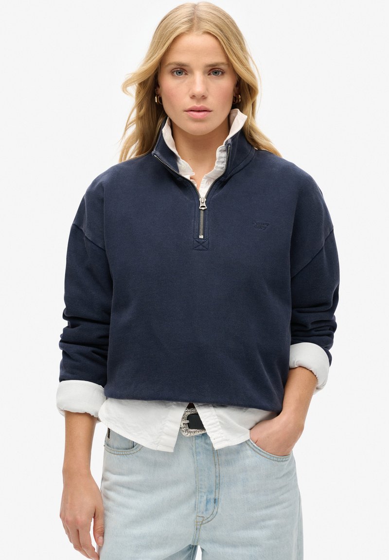 Marineblauwe half-zip pullover sweatshirt gemaakt van een zachte katoenmix, met verlaagde schouders en een witte blouse eronder.