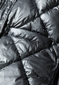 Melnā pūkainā jaka ar iešūtu, spīdīgu audumu. Iezīmēta ar diagonālu paneļu rakstu ar redzamām šuvēm, kas uzlabo tekstūru un dziļumu.