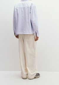Chemise oversize rayée bleu clair et blanche à manches longues, associée à un pantalon ample blanc et des baskets grises. Design simple et décontracté.