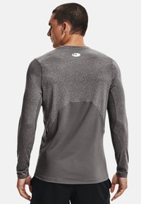 Langermet athletic skjorte i mørkegrå, med en teksturert overdel og glatt nedre panel, og en liten logo på nakken bak.
