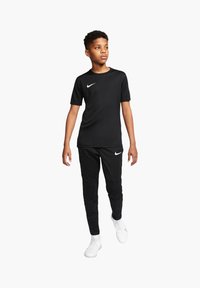 T-shirt nera Nike a maniche corte con logo bianco, abbinata a pantaloni jogger neri e sneaker bianche, caratterizzata da una vestibilità comoda e un design elegante.