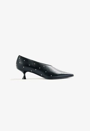 Zapato negro de cuero con puntera puntiaguda y tacón bajo tipo kitten, con pequeñas tachuelas plateadas distribuidas de manera uniforme en la superficie.
