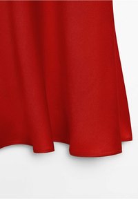 Tissu rouge vif avec des plis doux et une texture lisse, suspendu avec un ourlet légèrement évasé sur un fond blanc.