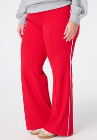 Red wide-leg pants made of soft fabric feature a contrasting white side stripe. Paired with beige footwear, shown against a plain background.