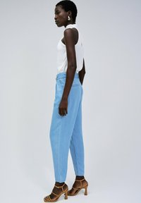 Jeans de tiro alto en azul claro, de corte relajado, con una textura limpia y suave. Combinados con una blusa sin mangas blanca y tacones marrones de tiras.