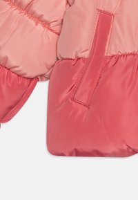 Pikowana kurtka w odcieniach różu i koralu, o gładkim satynowym wykończeniu, z marszczeniami oraz pętelką z materiału do zawieszania.