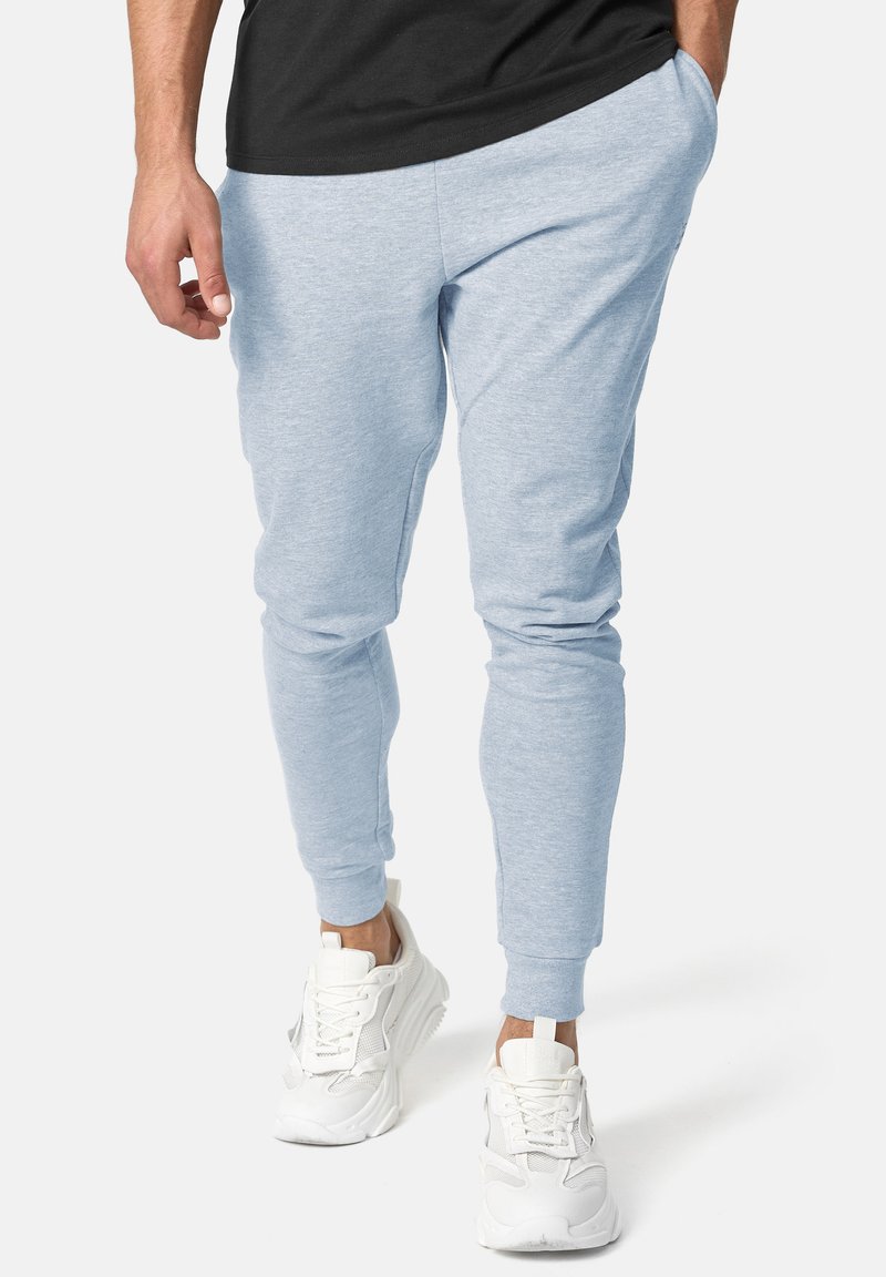 Helle blaue Jogginghose aus weichem Material, mit Seitentaschen und gerippten Bündchen; getragen mit weißen Sportschuhen.
