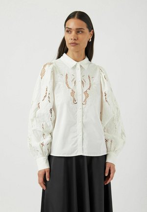 Hvit bluse med lange, puffede ermer som har broderte detaljer i blonder og en klassisk krage. Knapp foran og teksturerte detaljer.