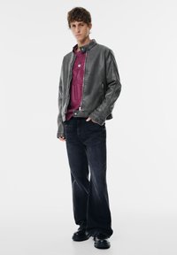 Grå faux læderjakke med høj krave, lagdelt over en maroon mønstret sweater, og parret med mørk denim flared bukser og sorte støvler.