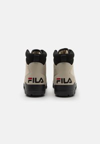 Stivaletti Fila beige e neri con colletto alto, superiore testurizzato e logo prominente sul tallone, dotati di suole in gomma per una buona aderenza.