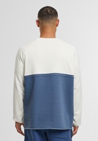 Lekki sweatshirt z białą górną częścią i niebieską dolną, z przeszywanym detalem szwu. Miękka tekstura i luźny krój.