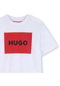 Vit bomulls-t-shirt med en framträdande rektangulär röd grafik med ordet "HUGO" i svart. Korta ärmar och rund halsringning.