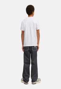Camiseta blanca de algodón y pantalones gris holgados con grandes bolsillos, con costuras en contraste y una textura suave. Incluye calzado casual.
