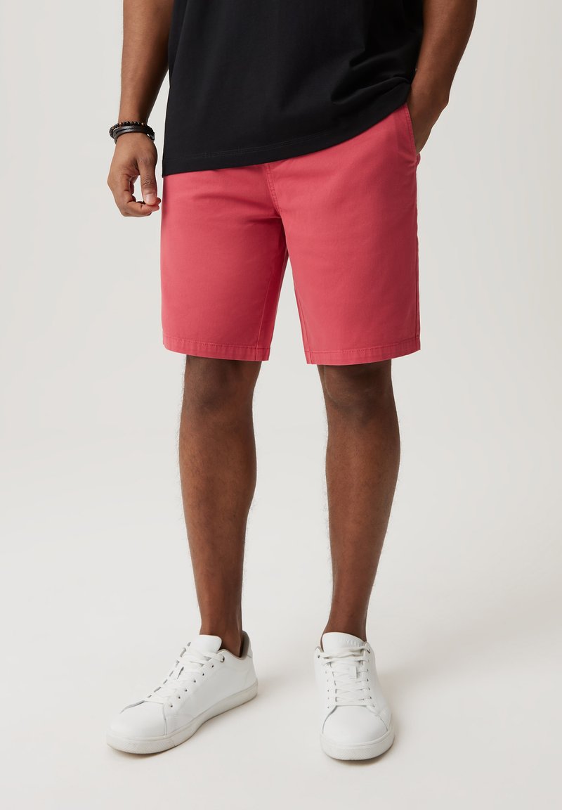 Czerwone bawełniane szorty o prostym kroju, z bocznymi kieszeniami i gładką fakturą, zestawione z białymi sneakersami w minimalistycznym designie.