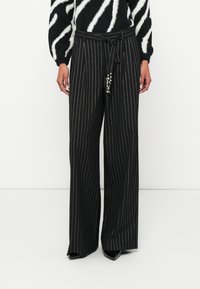 Pantalon rayé noir à jambes larges, doté d'une ceinture avec des accessoires décoratifs. Le tissu a une texture lisse et une coupe ajustée.
