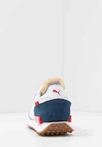 Retro tenisky s bílým koženým svrškem, námořnicky modrými semišovými detaily, červenými kovovými prvky a texturovanou gumovou podrážkou pro lepší přilnavost.