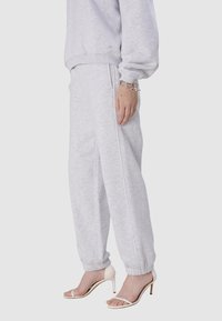 Helle graue Jogginghosen aus weichem Material mit elastischen Bündchen, kombiniert mit weißen, schmalen High Heels. Verfügt über dezentes Branding am Bund.